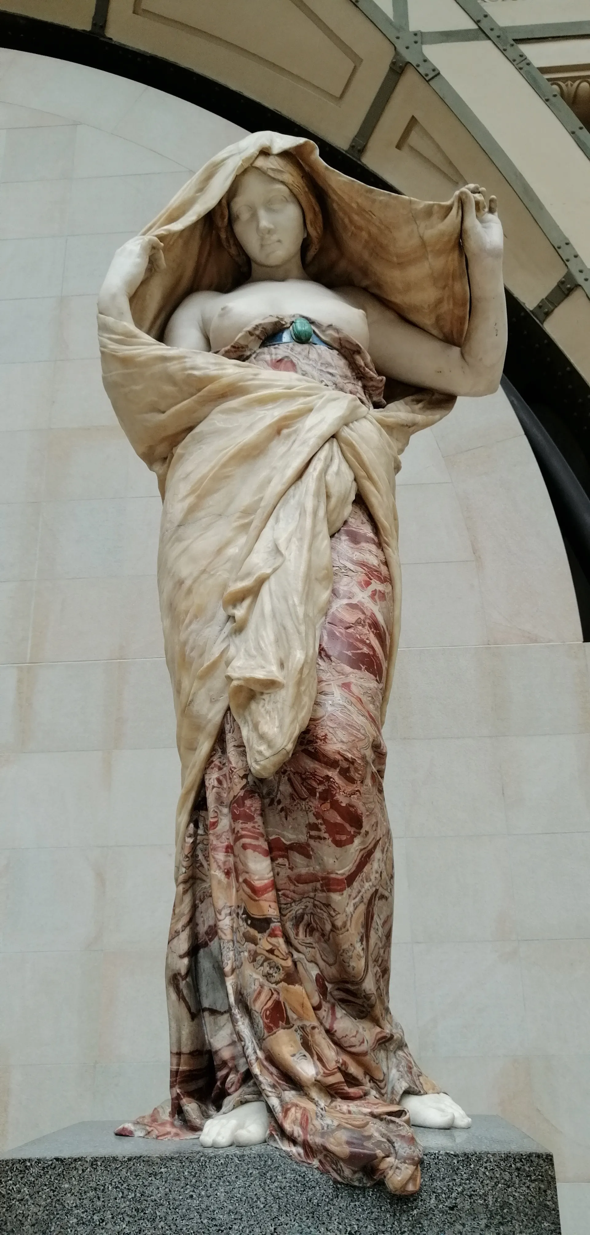 A marble statue of a woman wrapped in a patterned cloak.