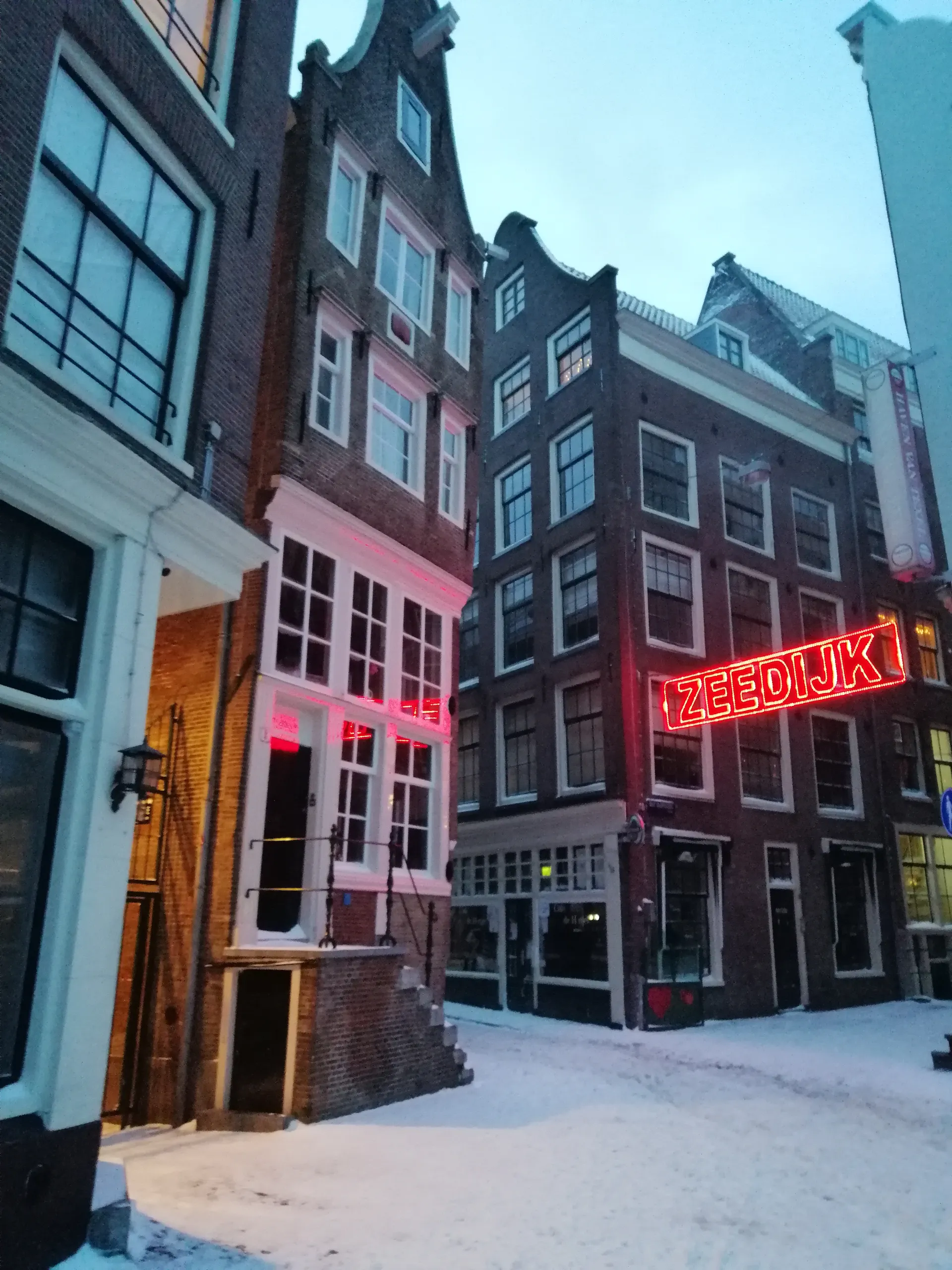 Canal houses and a neon sign above a snow-covered street.