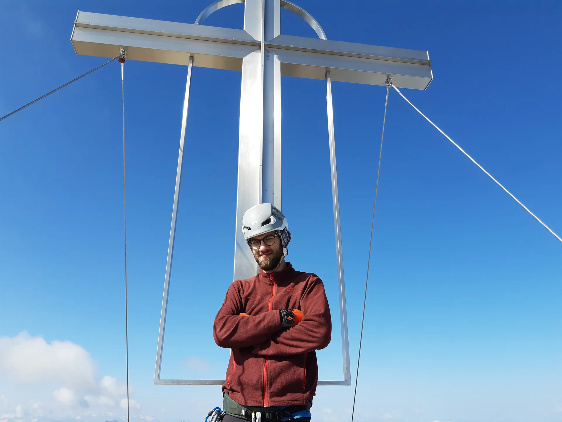Standing under a metal summit cross against a deep blue sky.
