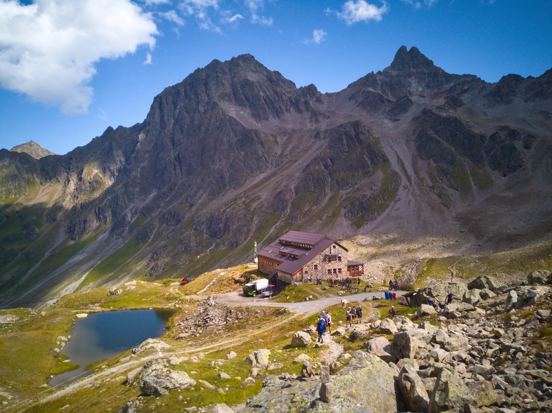 A mountain hut beside a small lake below jagged rock peaks.