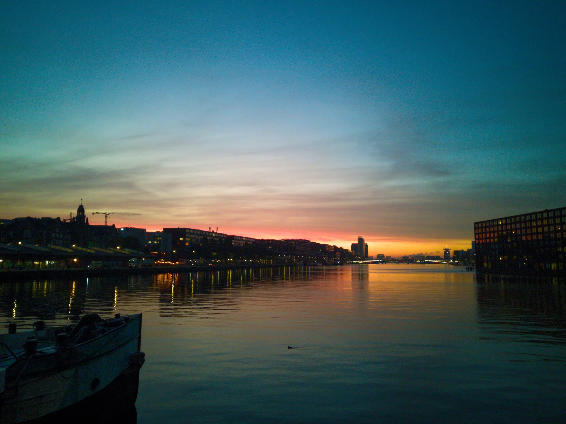 Dusk over a wide harbour with the city skyline on the horizon.