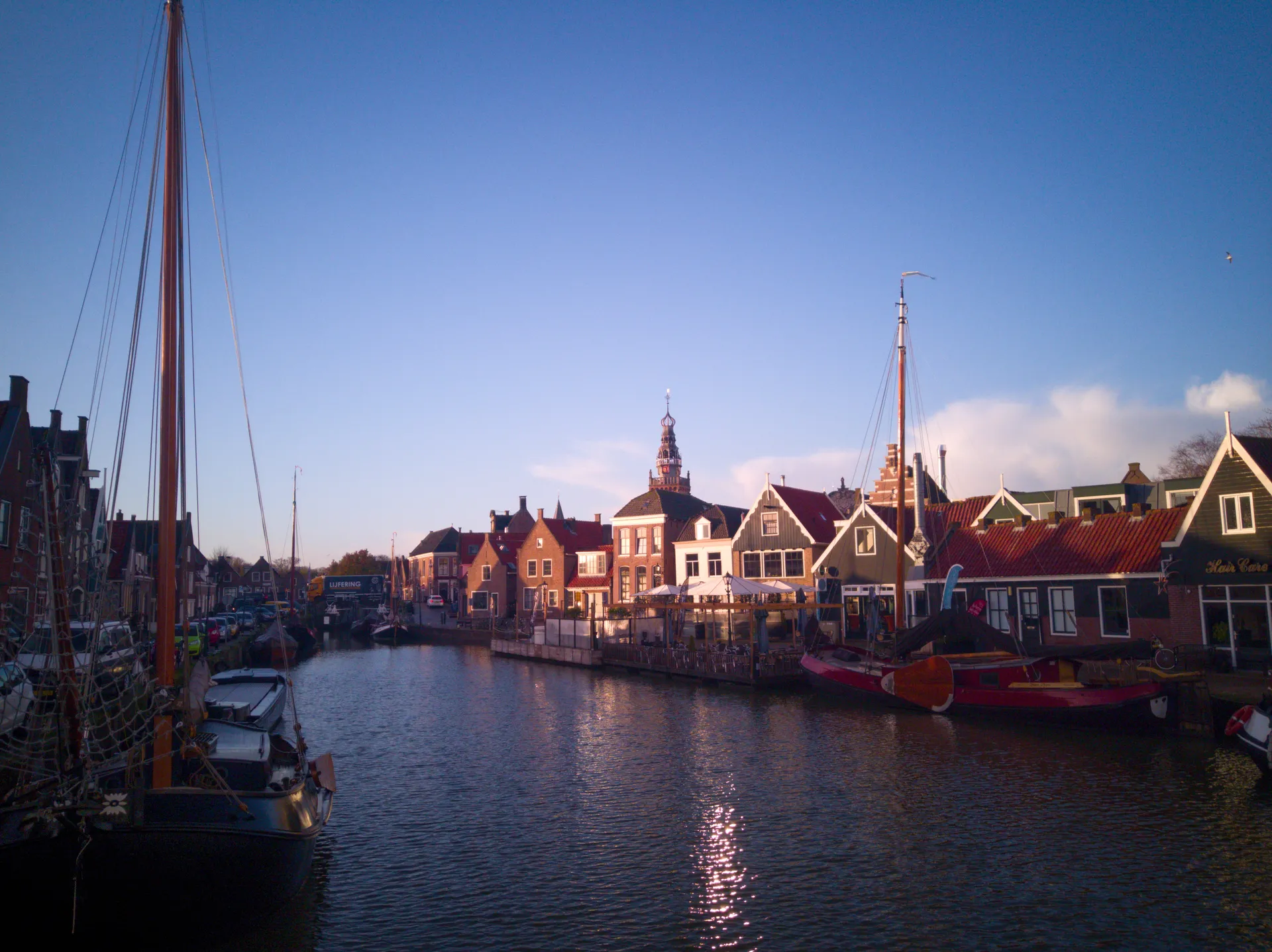 Sailing boats moored in front of gabled houses in the morning light.