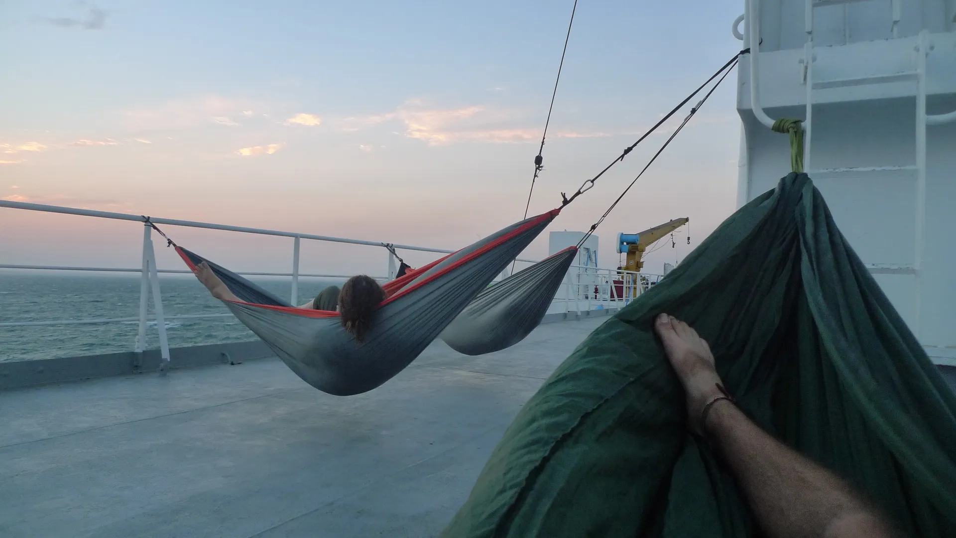 Hammocks strung between the rails on the deck of a ferry at sea.