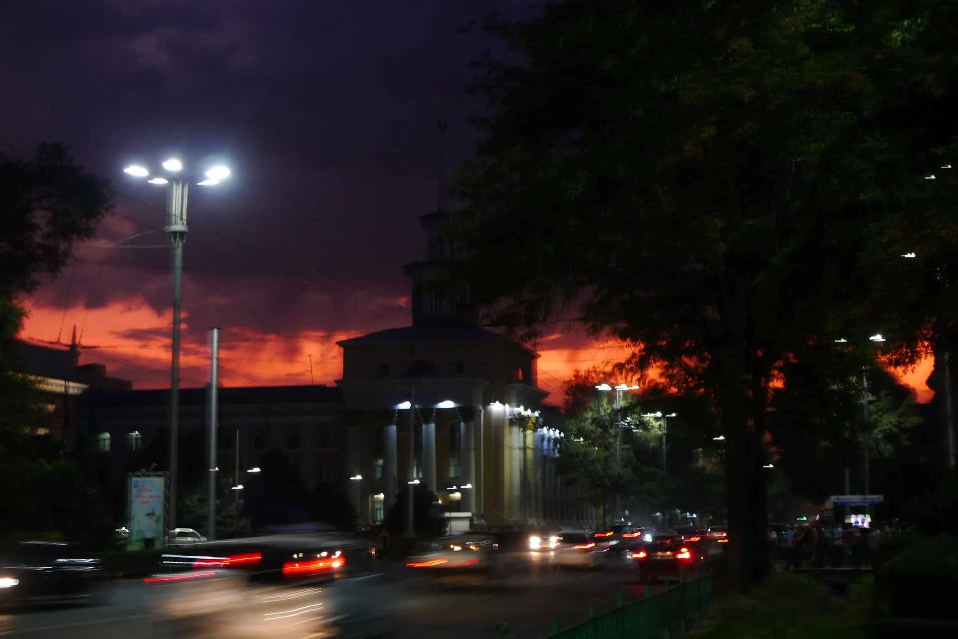 A burning red sky behind street lights and a busy avenue.
