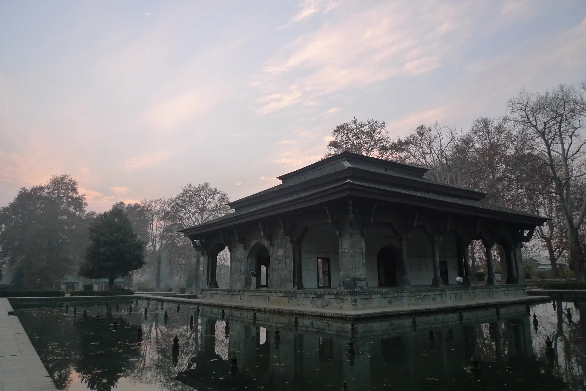 A wooden pavilion reflected in still water at dusk.