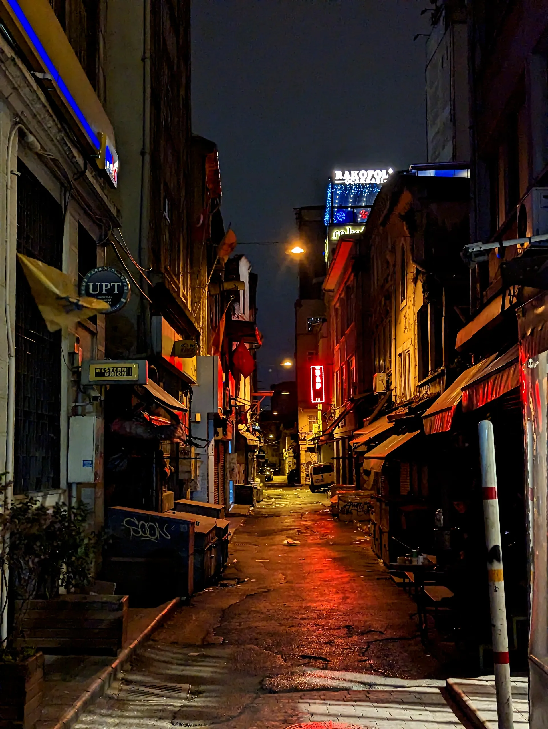 A narrow street glowing with shop lights after rain.