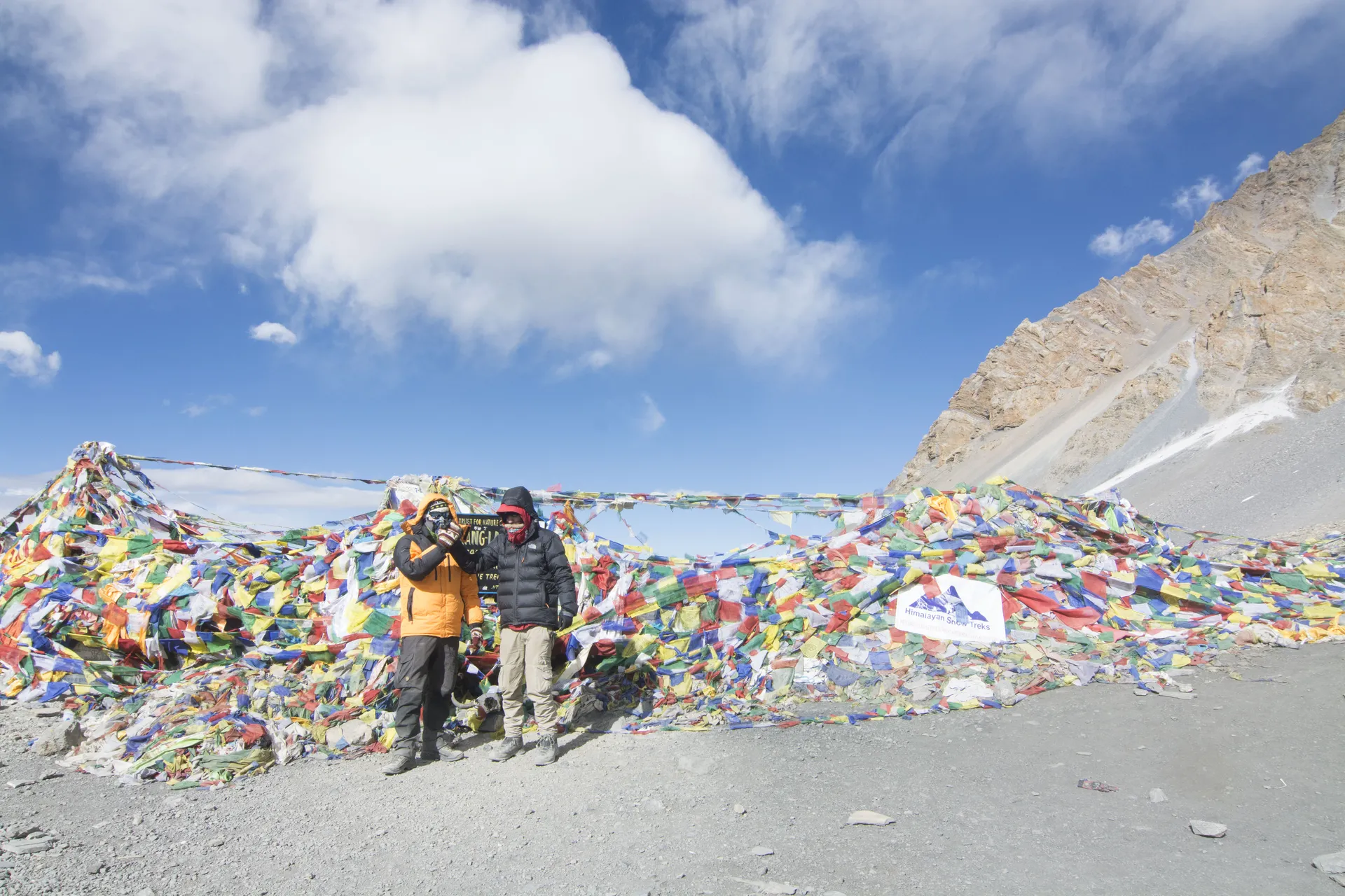Two climbers in front of a pile of prayer flags on a high pass.